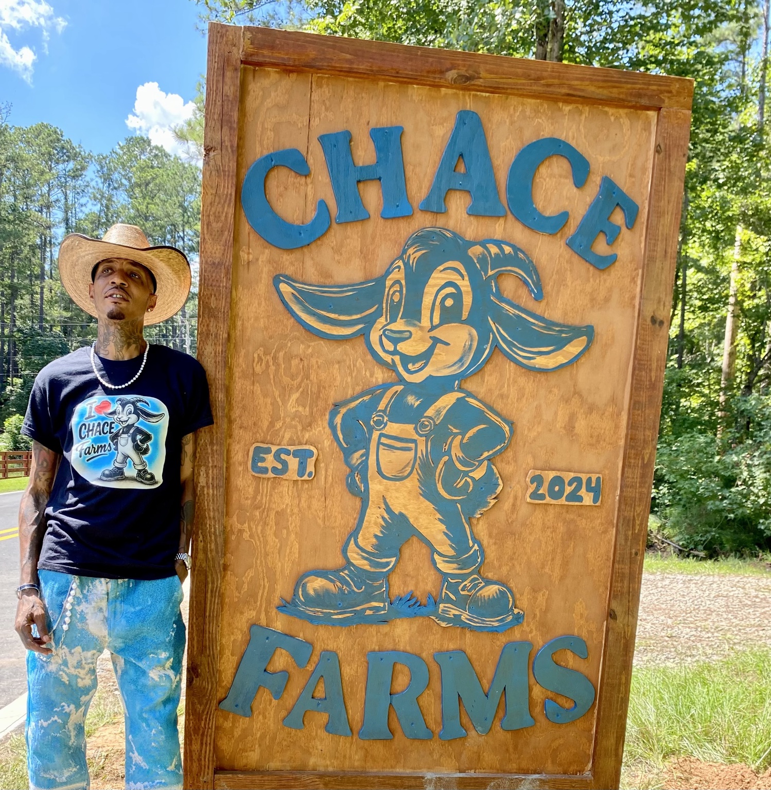 A person in a straw hat beside the wooden CHACE Farms sign, surrounded by trees