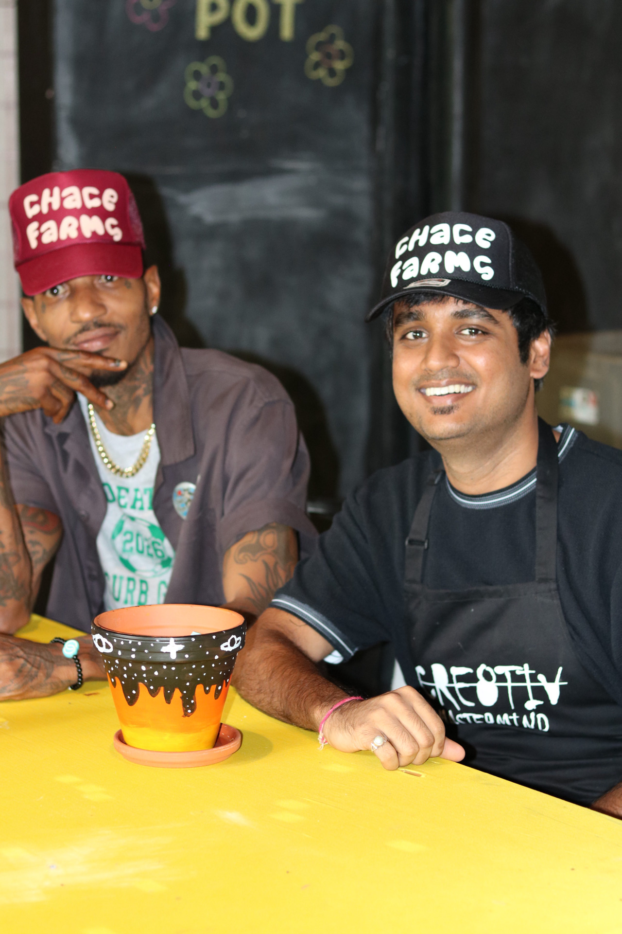 Two event participants wearing CHACE Farms hats beside a painted flowerpot