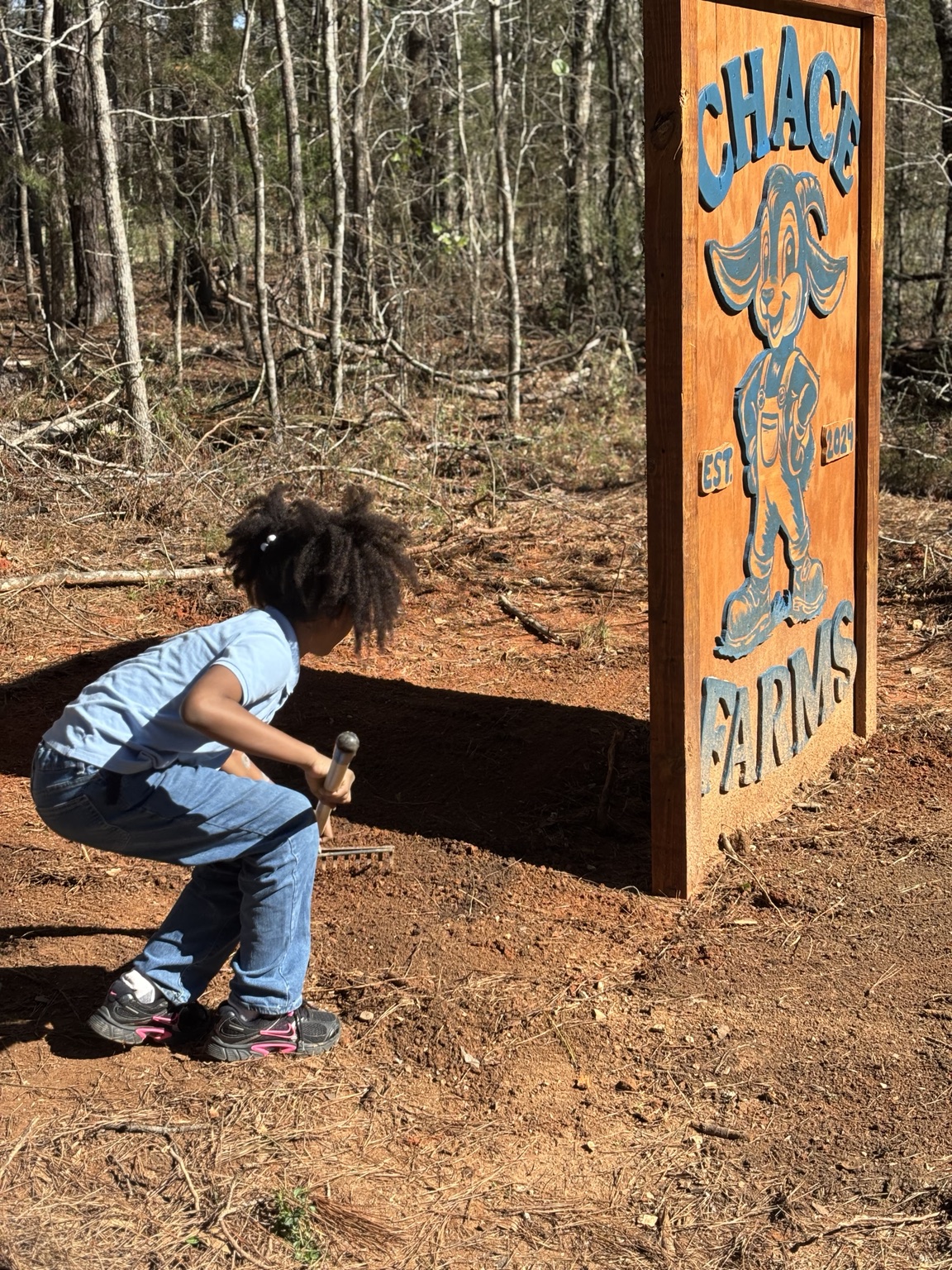 A young volunteer tending the ground beside the wooden CHACE Farms sign